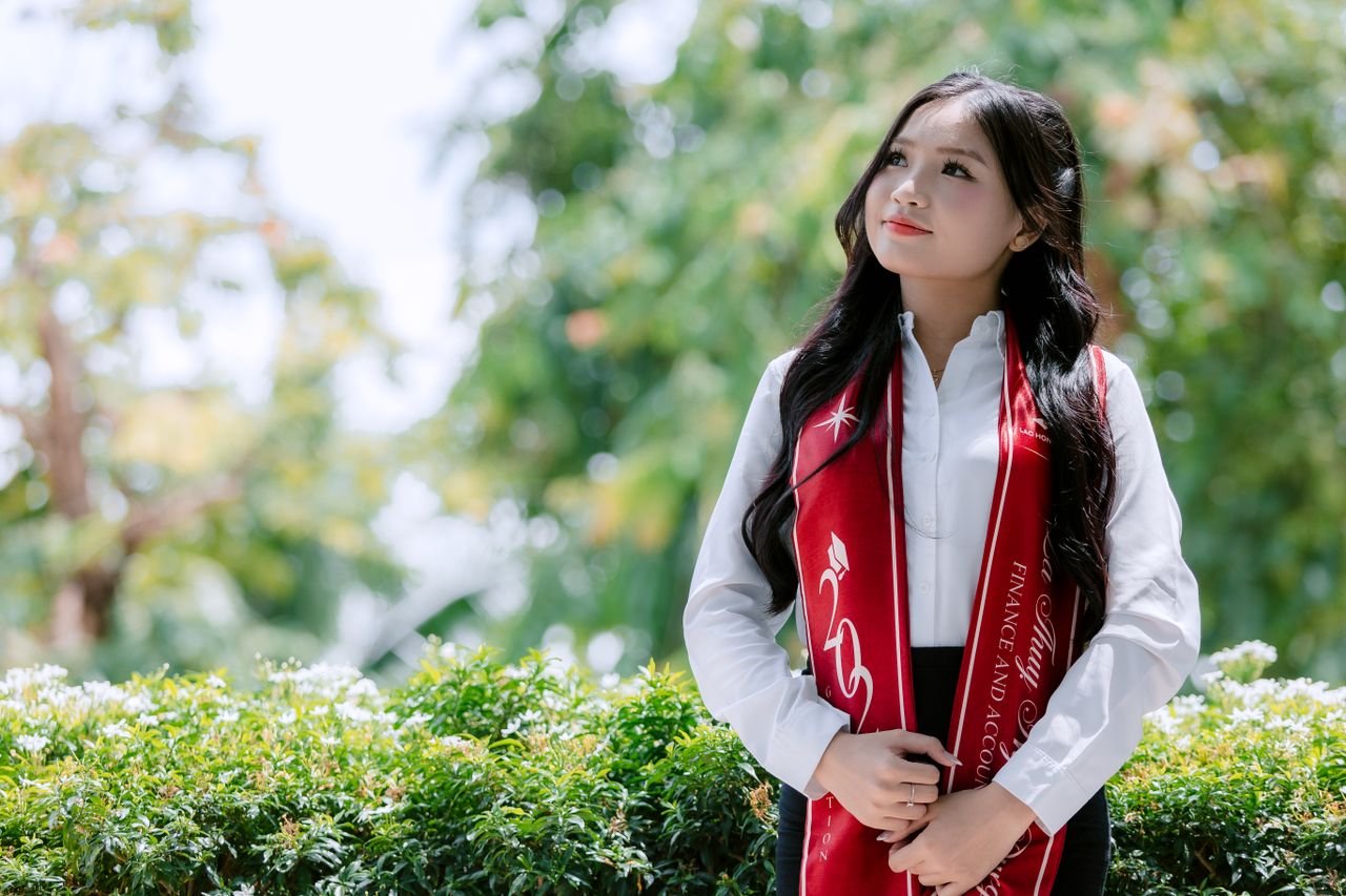 Proud young graduate wearing red stole in garden setting on a bright day.