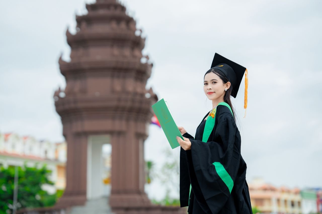 A young Cambodian graduate smiles in a cap and gown at a ceremony in Krong Battambang.