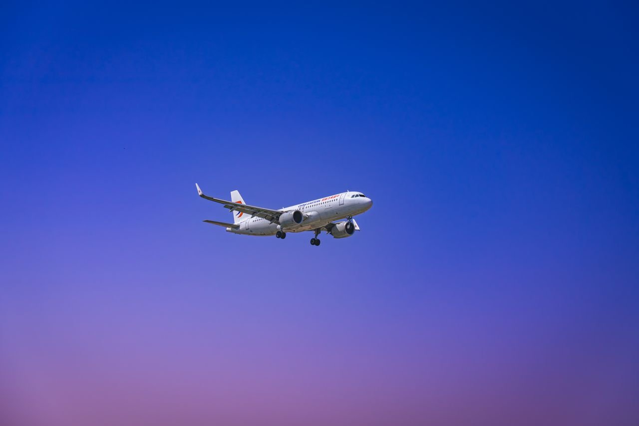 A commercial airplane flying through a clear blue and purple sky during daytime.